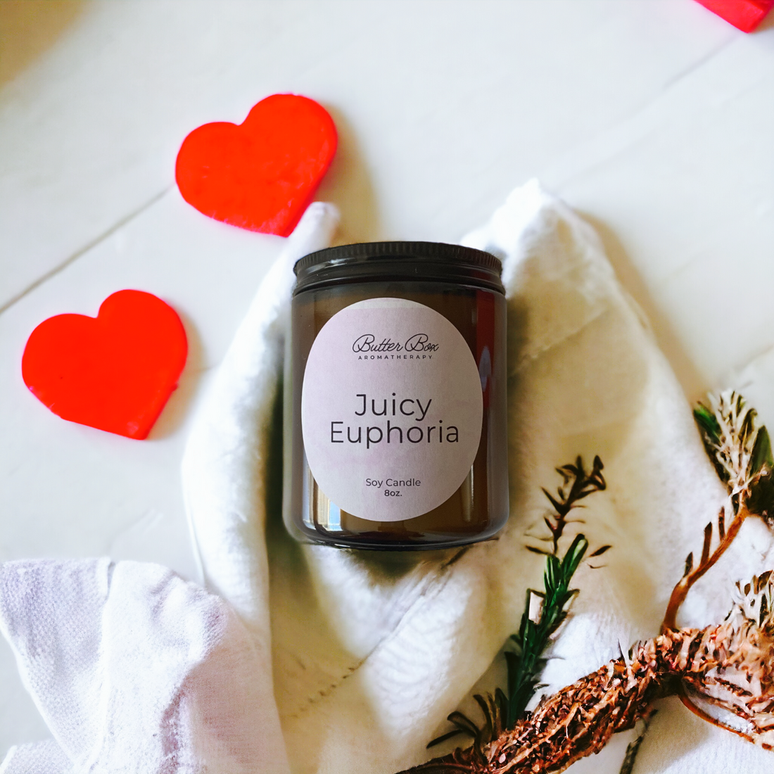 two red hearts with Juicy Euphoria candle jar with white cloth underneath
